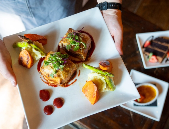 A plate with Beef Wellington in the foreground with some soup and cake in the background