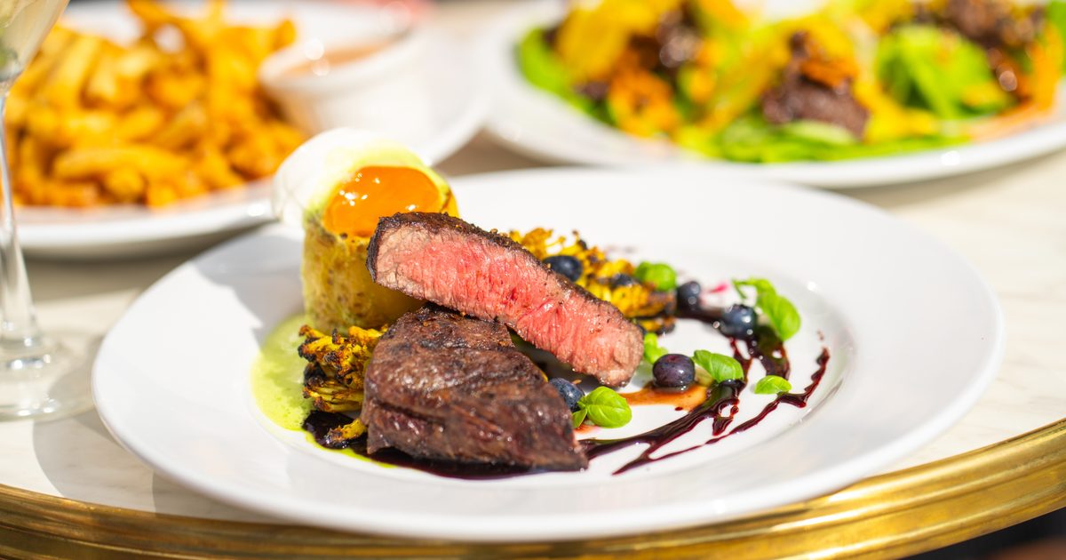 A nice steak supper with plates of fries and other sides in the background