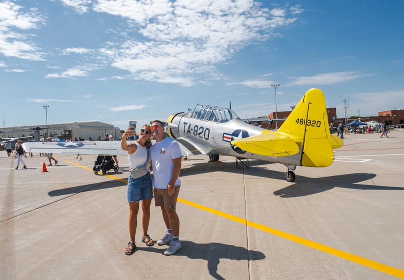 Two people taking a picture in front of a plane at the Sioux Falls Airshow